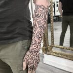 A person's arm and hand covered in a detailed Nordic style knotwork tattoo.