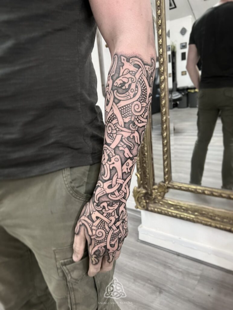 A person's arm and hand covered in a detailed Nordic style knotwork tattoo.