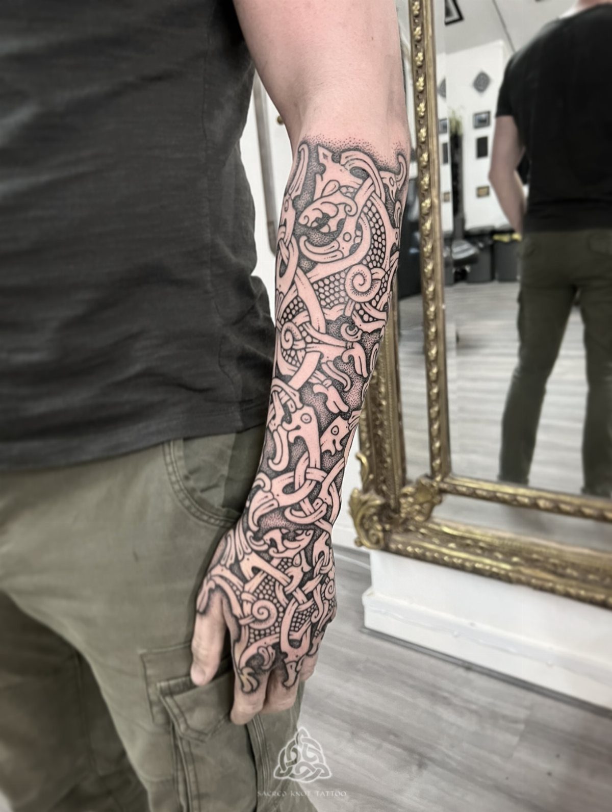 A person's arm and hand covered in a detailed Nordic style knotwork tattoo.