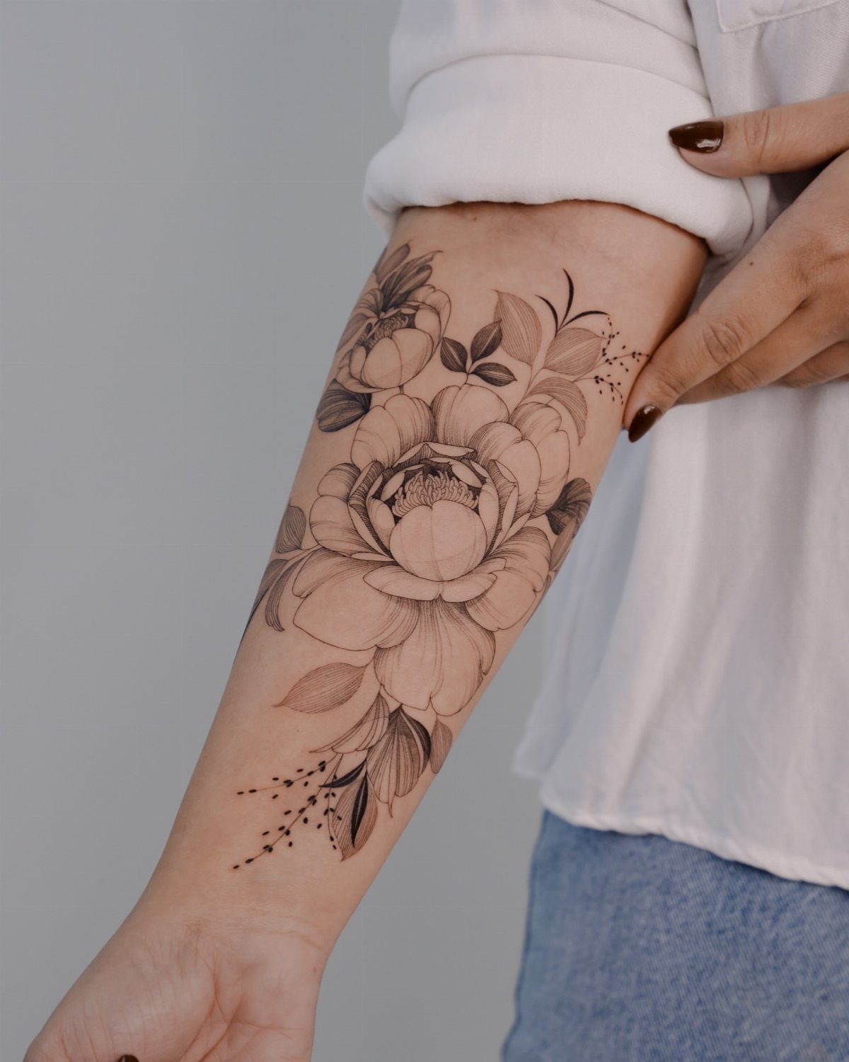 A large black ink floral tattoo of a peony with leaves on a person's forearm.