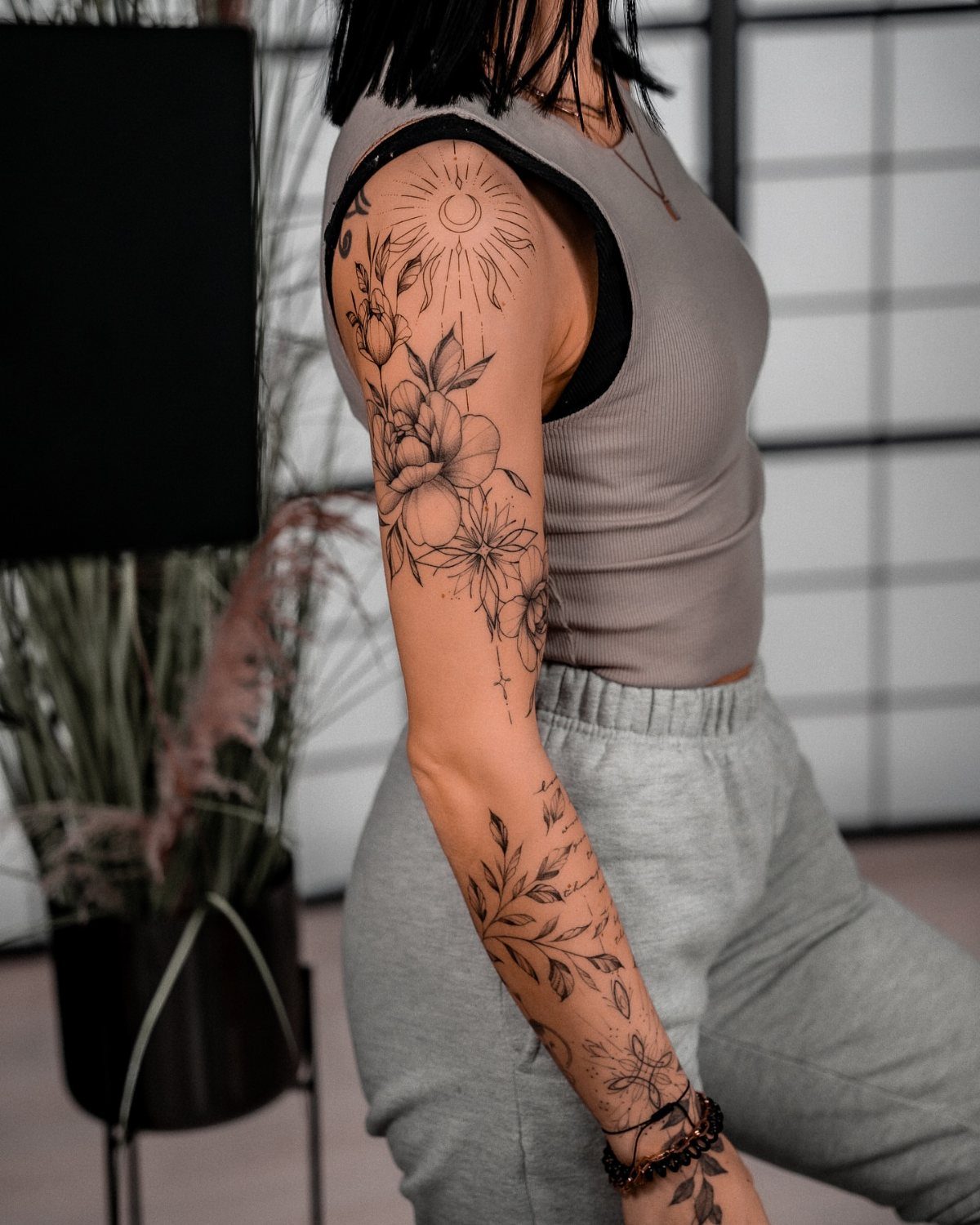 A person's arm displaying a detailed fine line tattoo sleeve with flowers and sun motifs.