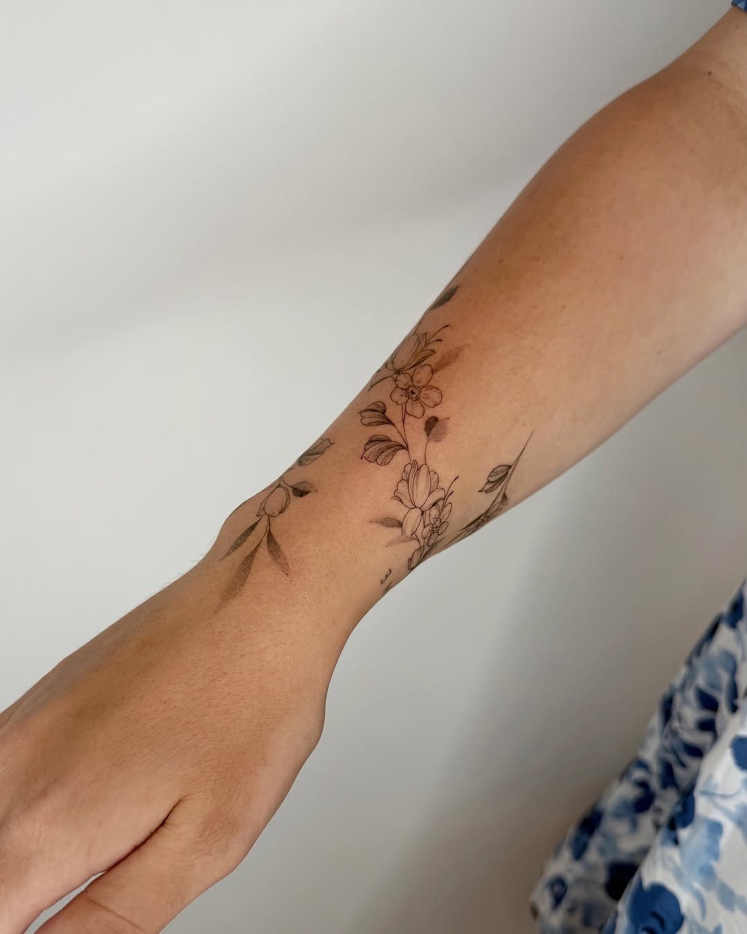A forearm with a delicate black ink floral wrap around tattoo design.
