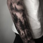 A detailed black and grey forest landscape tattoo covering a person's forearm.