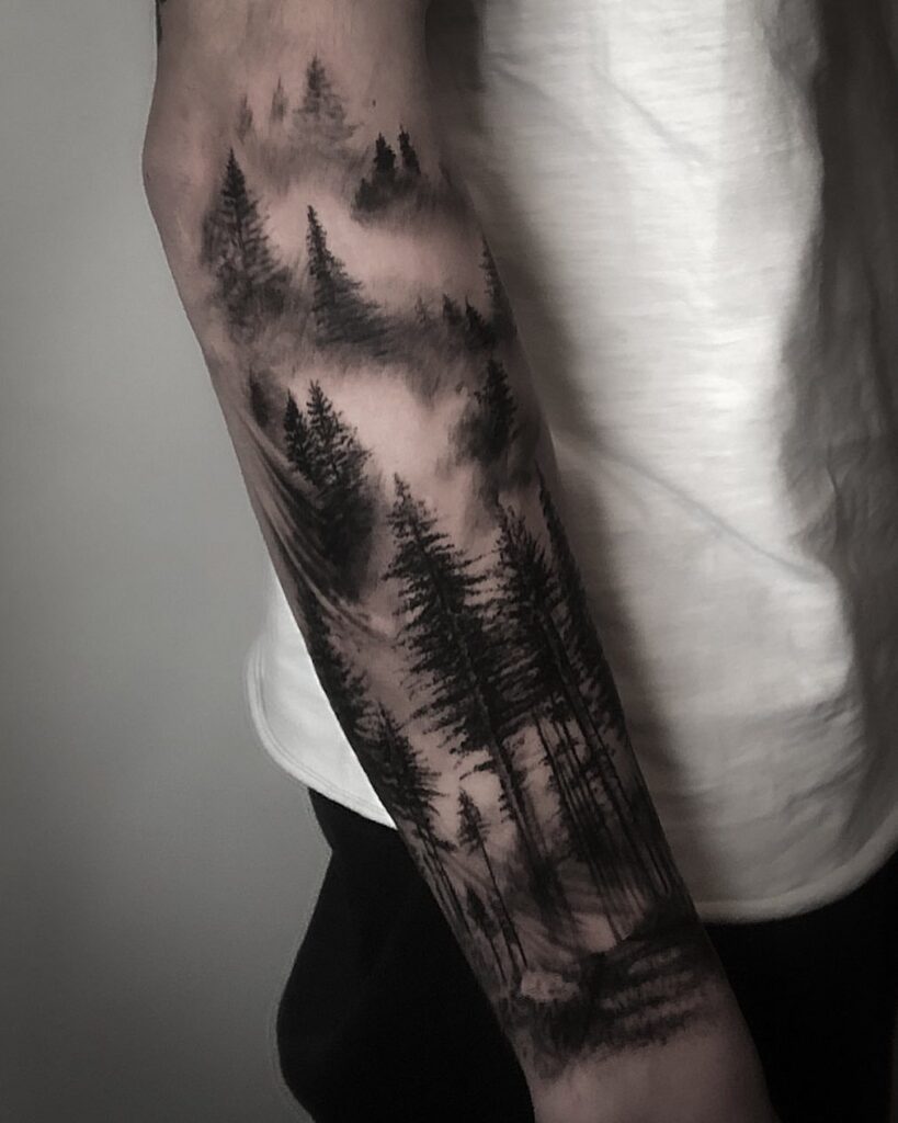 A detailed black and grey forest landscape tattoo covering a person's forearm.