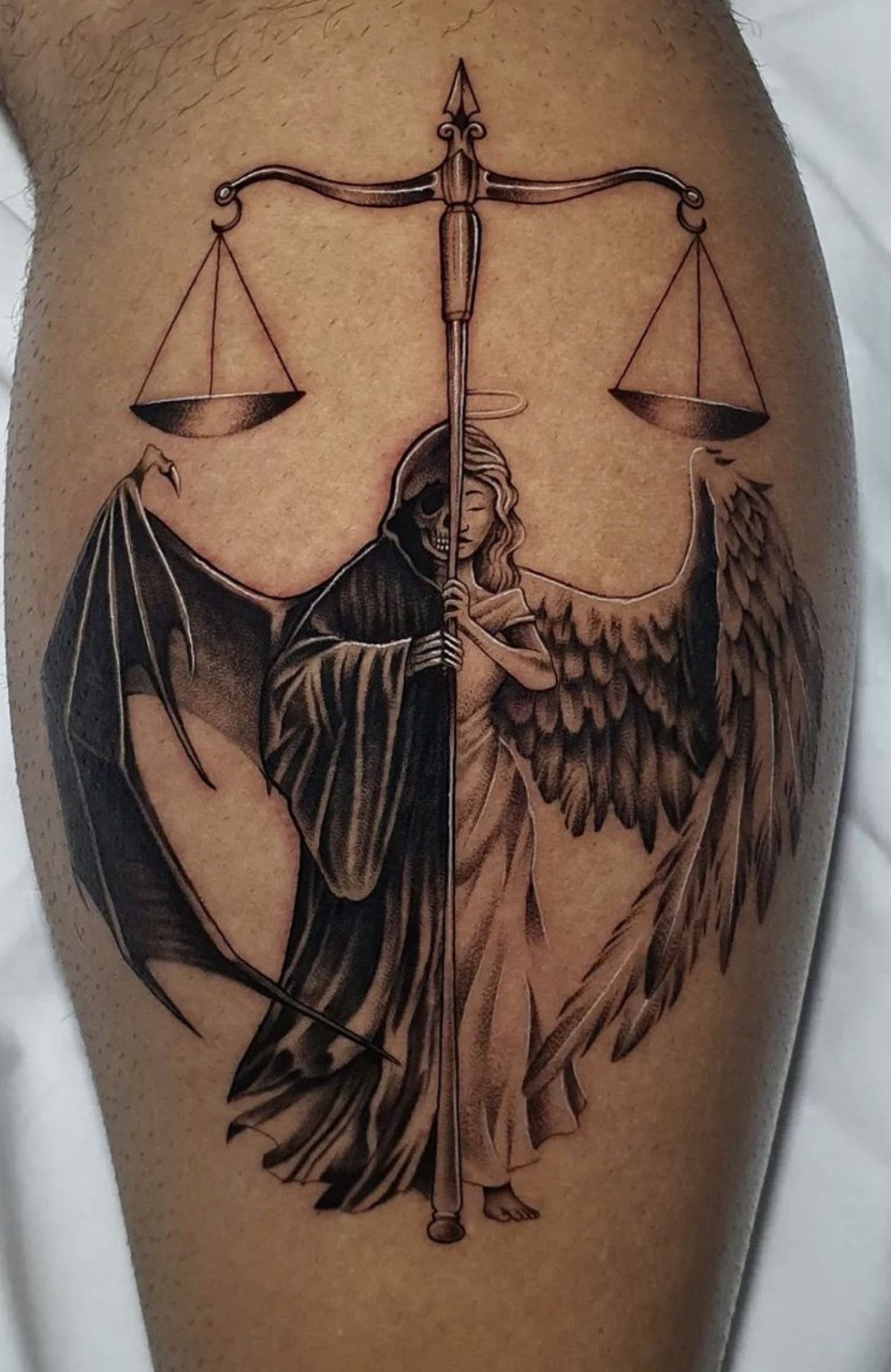 A black and grey tattoo of a hooded figure with one angel wing and one bat wing.