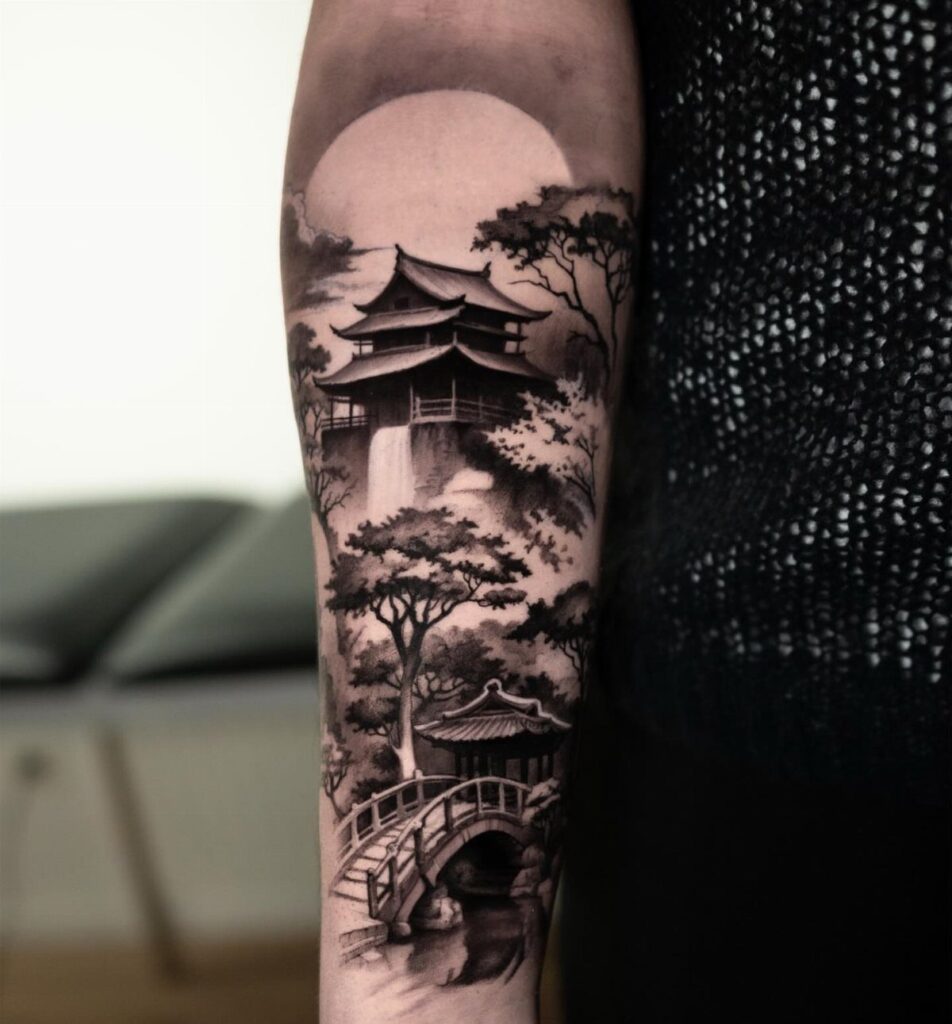 A black and grey tattoo on an arm showing a Japanese landscape with a pagoda, bridge, and sun.