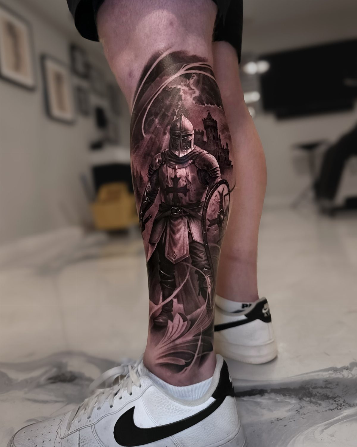 A detailed black and grey knight tattoo covering a person's lower leg.