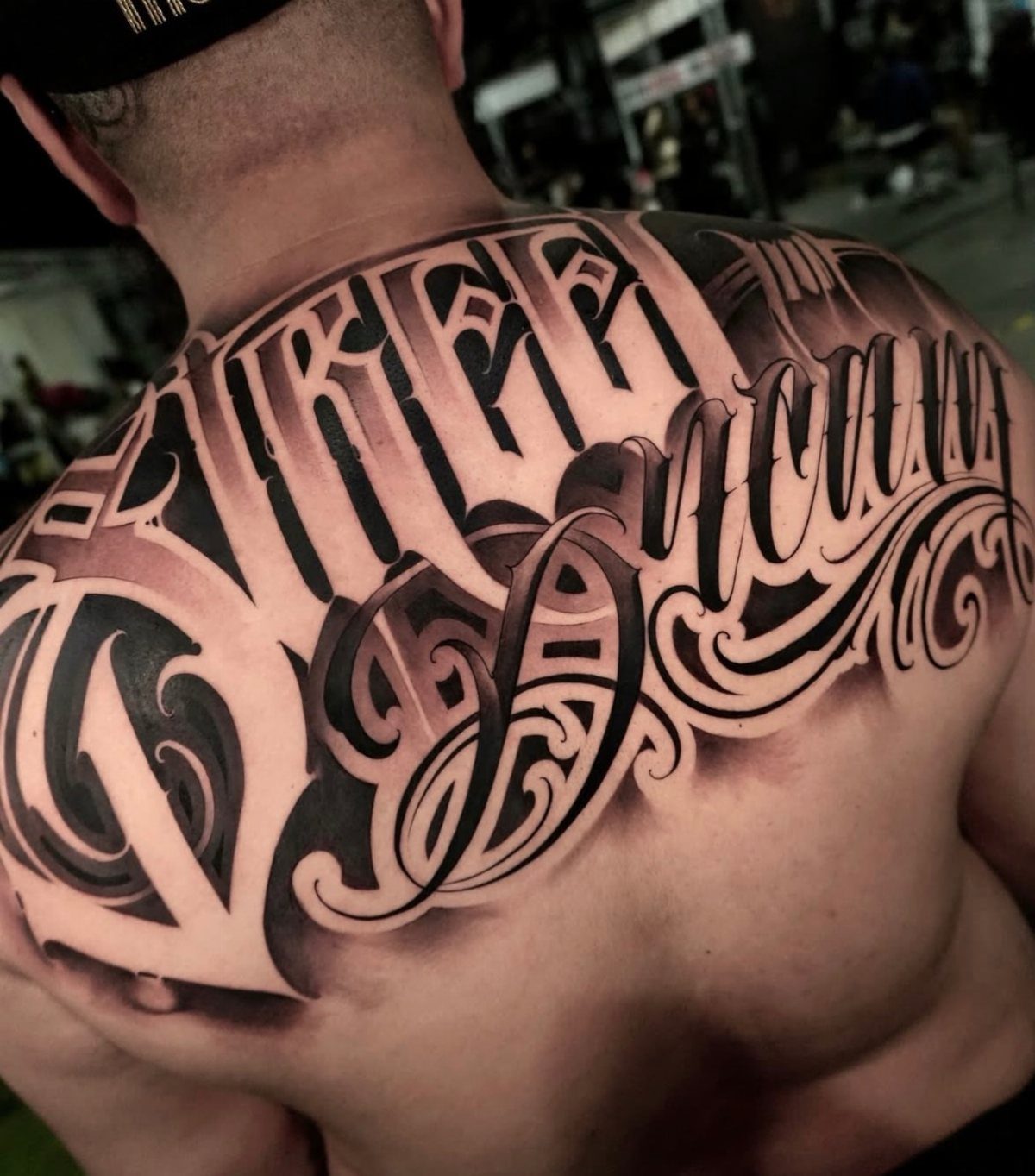 Large black and grey script tattoo covering a person's upper back and shoulders.