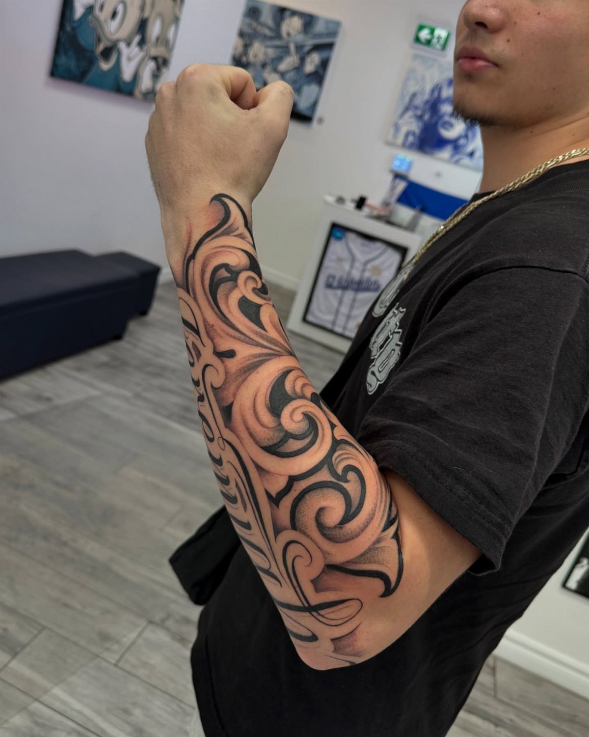 A man's arm displaying a large black and grey ornamental filigree tattoo design.