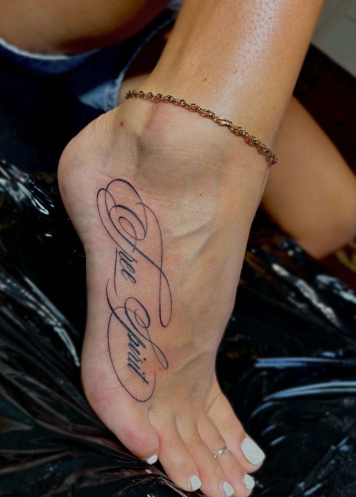 A foot with a black script tattoo reading Free Spirit and white painted toenails.