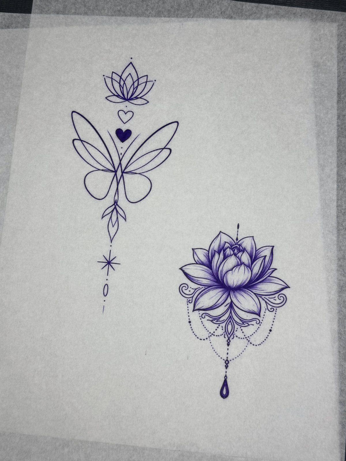 Two purple ink tattoo designs featuring a butterfly and a lotus on transfer paper.