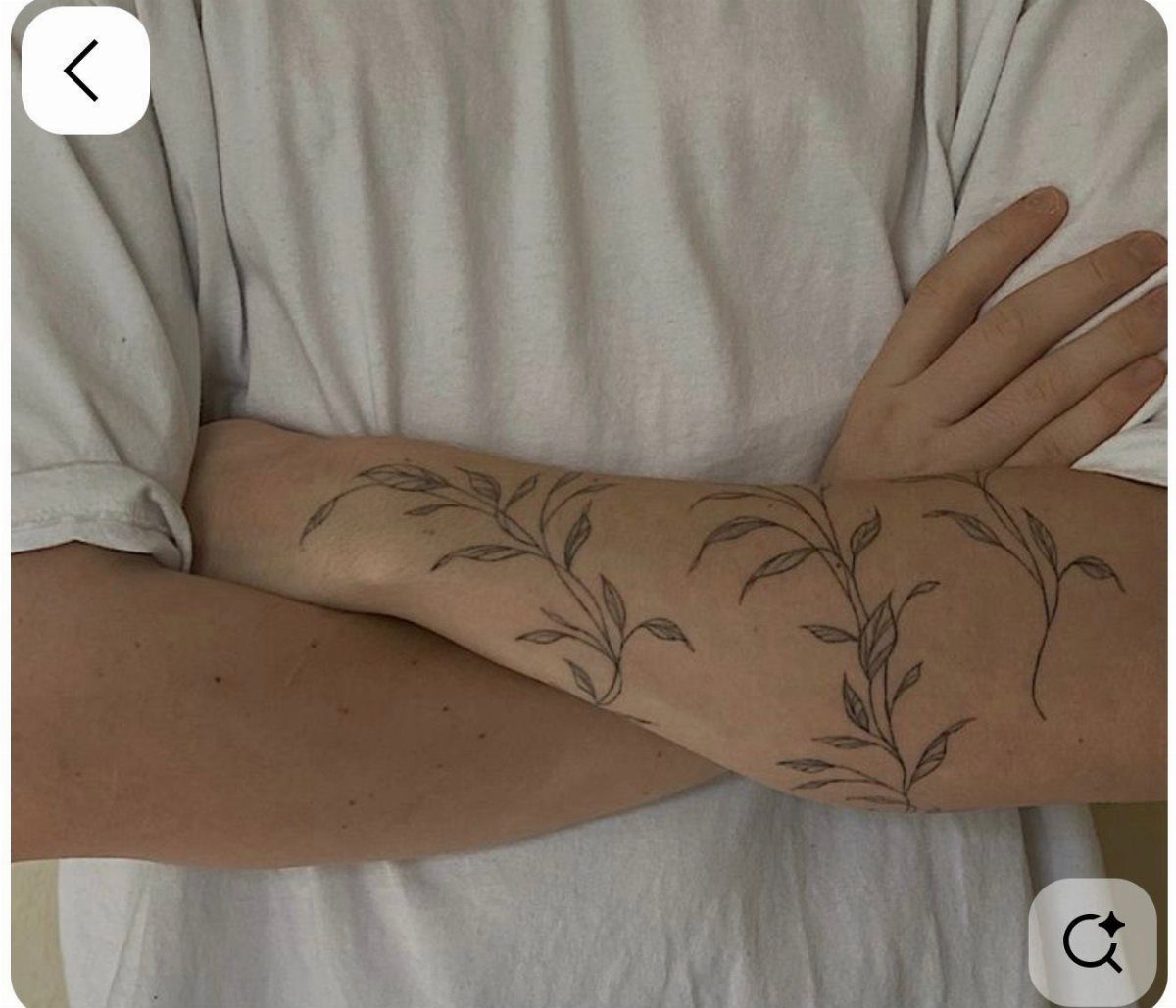 A forearm with a delicate vine and leaf tattoo wrapping around the skin.