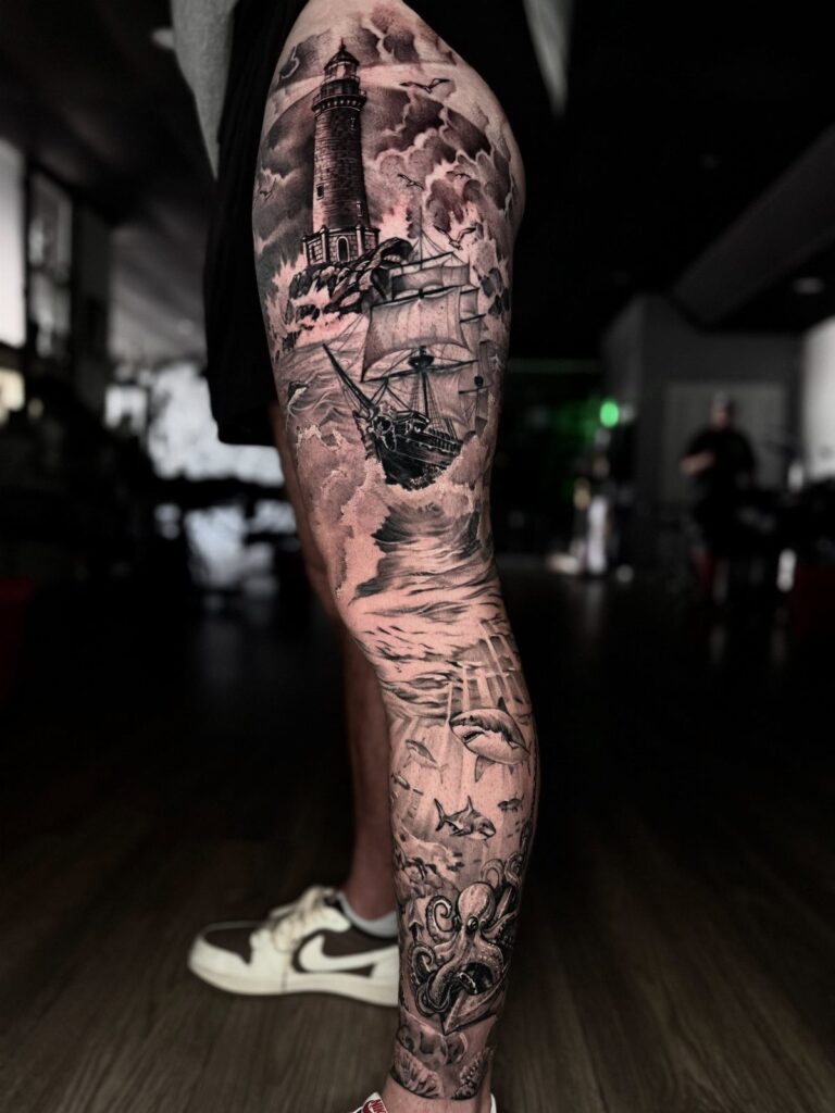 A detailed black and grey leg tattoo depicting a lighthouse, sailing ship, and octopus.