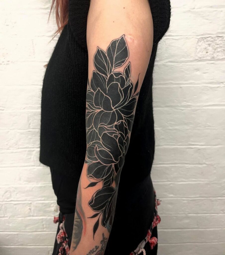 Large black and grey floral tattoo covering a person's arm against a white brick wall.