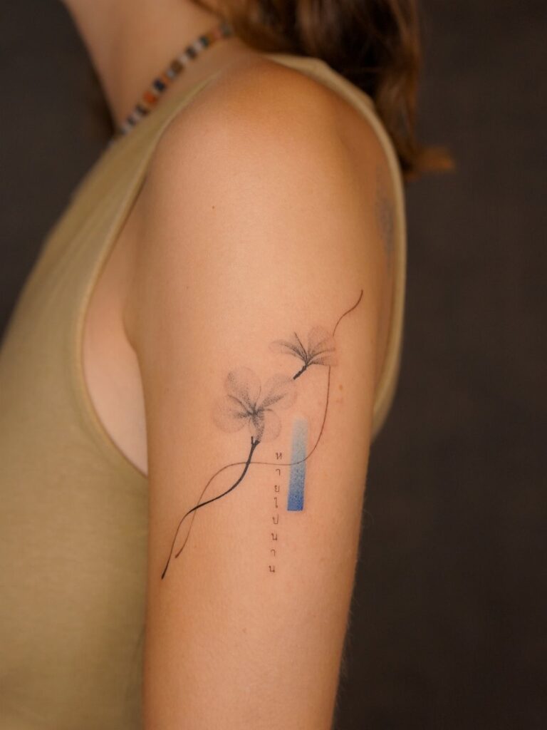 A minimalist floral tattoo with thin black lines and blue accents on a person's arm.
