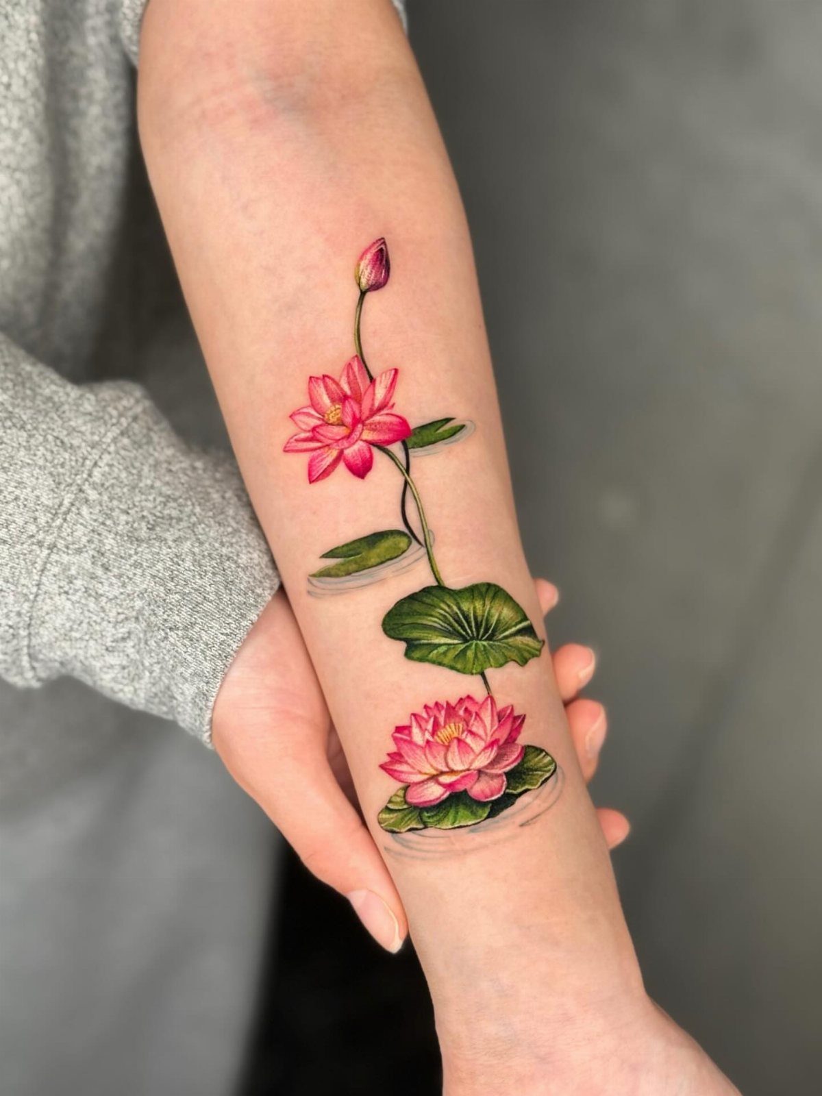 A vibrant pink water lily tattoo with green leaves on a person's forearm.